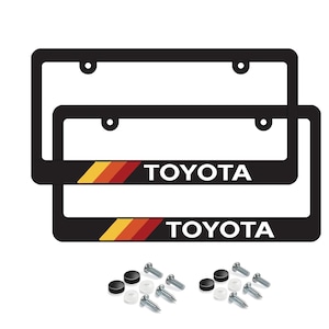 May include: Two black license plate frames with the word "TOYOTA" in white. The frames have a stripe of yellow, orange, and red. Mounting hardware is included.