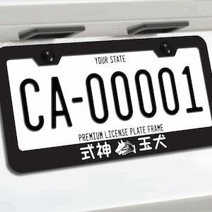 Puede incluir: Marco de matrícula negro con una placa blanca. La placa dice "CA-00001" en fuente negra. El marco tiene el texto "YOUR STATE" y "PREMIUM LICENSE PLATE FRAME". Texto japonés y un gráfico de perro en la parte inferior.