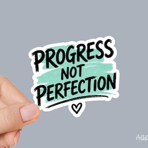 May include: A die-cut sticker featuring the black text PROGRESS NOT PERFECTION layered over a light mint green watercolor brushstroke background. A small black hand-drawn heart icon is positioned directly below the text on a white border.