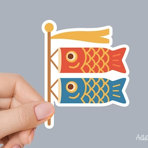May include: A sticker featuring two stylized koi fish windsocks, one red and one blue, on a wooden pole with a yellow banner. The fish have detailed scale patterns and are set against a light gray background.