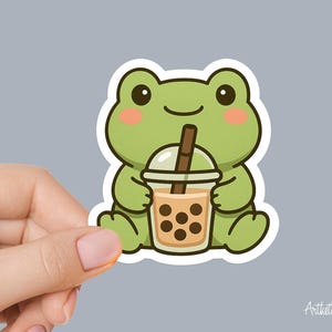 May include: A sticker featuring a cartoon frog holding a bubble tea. The frog is green with pink cheeks and a white outline. The bubble tea is in a clear cup with a brown straw and brown tapioca pearls. The sticker has a white border.