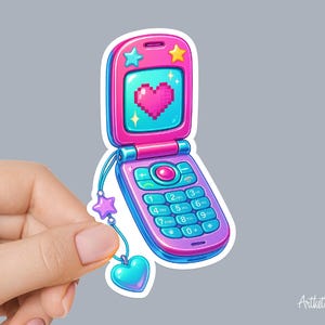 May include: A sticker of a pink and blue flip phone with a pixelated heart on the screen. The phone has a star and heart charm attached. The phone's design is reminiscent of early 2000s technology.