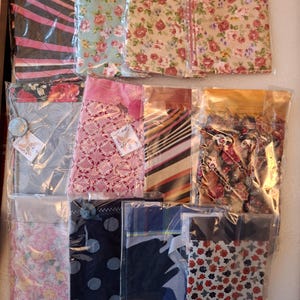 May include: An assortment of fabric pouches in various floral and patterned designs. The pouches are packaged in clear plastic, showcasing the different colors and styles, including stripes, polka dots, and floral prints. Each pouch has a tag attached.