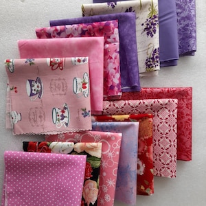 May include: A stack of 10 fabric squares in various shades of pink, purple, and red with different patterns. The patterns include floral designs, polka dots, and geometric shapes. The fabric squares are arranged in a staggered pattern, with the largest square at the bottom and the smallest square at the top.