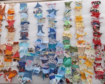 May include: Rows of colorful fabric pieces in various patterns and colors, including orange, blue, green, yellow, and red. The fabric pieces are arranged in vertical lines, possibly for a quilting project or textile art.