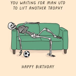 May include: A humorous birthday card featuring a cartoon skeleton lounging on a green couch with a soccer ball. The card reads "YOU WAITING FOR MAN UTD TO LIFT ANOTHER TROPHY" and "HAPPY BIRTHDAY" in black text on a beige background.