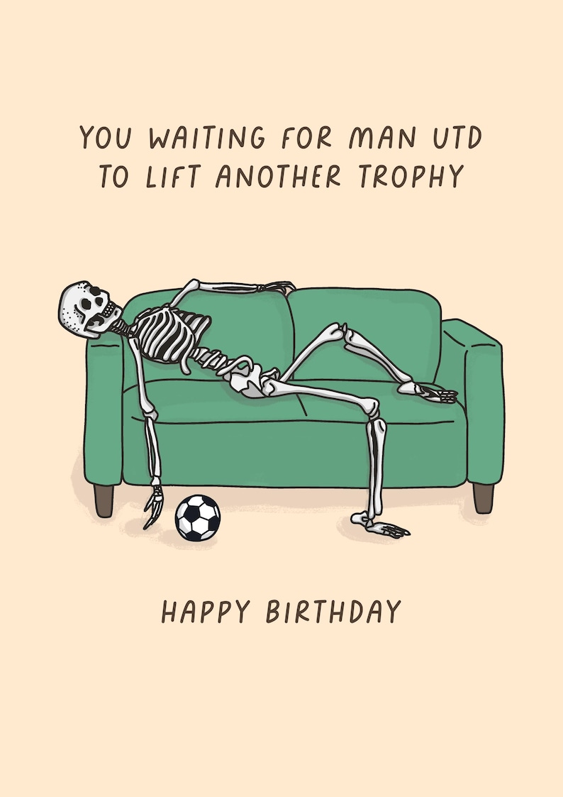 May include: A humorous birthday card featuring a cartoon skeleton lounging on a green couch with a soccer ball. The card reads "YOU WAITING FOR MAN UTD TO LIFT ANOTHER TROPHY" and "HAPPY BIRTHDAY" in black text on a beige background.