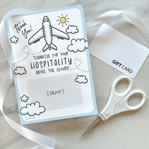 Może przedstawiać: Karta podarunkowa z niebieską obwódką, samolotem, chmurami i ilustracją słońca. Tekst zawiera "Thank You!" i "Thankful for your Hospitality Above the Clouds!". Obecna jest również biała karta podarunkowa i nożyczki.