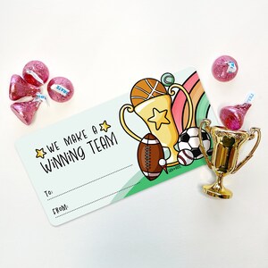 Könnte beinhalten: Ein grünes und weißes Geschenkanhänger mit einer Cartoon-Illustration einer Trophäe, eines Basketballs, eines Fußballs, eines Fußballs und eines Baseballs. Das Etikett lautet "We make a winning team" und hat Platz zum Schreiben von "To:" und "From:".