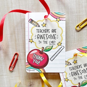 Può includere: Un'etichetta regalo bianca con la scritta "TEACHERS ARE AWESOME TO THE CORE!" e "THANK YOU!" stampata sopra. L'etichetta presenta una mela rossa, una matita, un righello e delle stelle. Sono visibili anche un nastro rosso e una graffetta rossa.