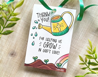 May include: A white gift tag with a green ribbon, featuring a hand-drawn illustration. The tag says "THANK YOU!" and "FOR HELPING US GROW IN GOD'S LOVE!" A yellow watering can with a cross is depicted, along with a rainbow and sprouting plants.