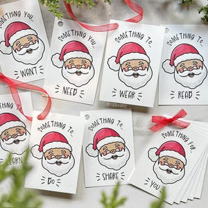 Pode incluir: Etiquetas de presente brancas com uma ilustração do Papai Noel com chapéu e barba vermelhos. As etiquetas trazem frases como "Something You Want", "Something to Wear" e "Something for You". Fita vermelha anexada.