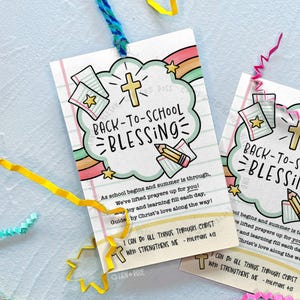 May include: A rectangular paper tag featuring a light green cloud graphic with the text BACK-TO-SCHOOL BLESSING, a yellow cross, a pencil, and lined paper. The tag includes a prayer, the verse Philippians 4:13, and a blue yarn loop at the top.