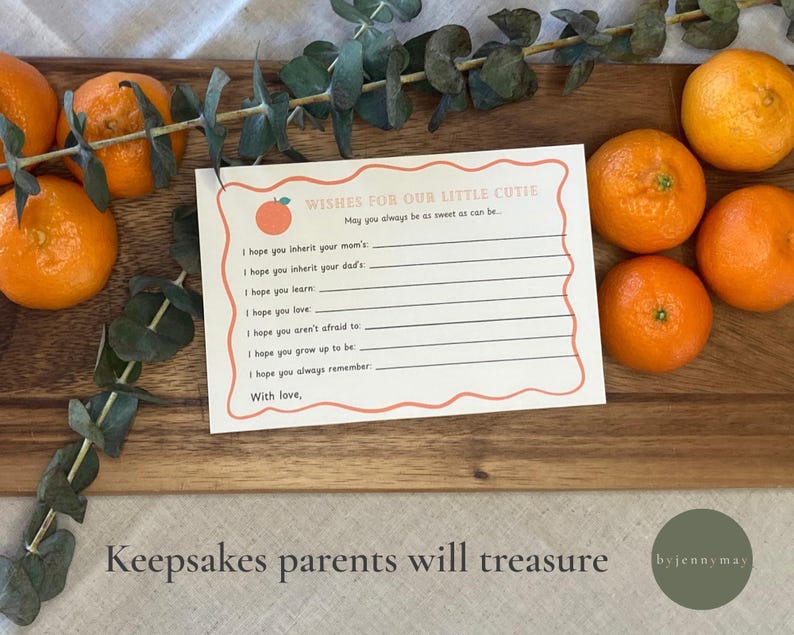May include: A card with the text "Wishes for Our Little Cutie" and lines for writing, surrounded by oranges and eucalyptus. The card sits on a wooden board. The image also includes the text "Keepsakes parents will treasure".