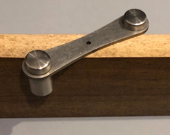May include: A silver metal bracket with two round knobs on a wooden surface.