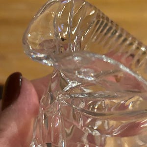 Op de afbeelding: Close-up van een heldere glazen kan met een decoratief, facetgeslepen ontwerp. De kan heeft een brede, uitlopende opening en een ronde basis.