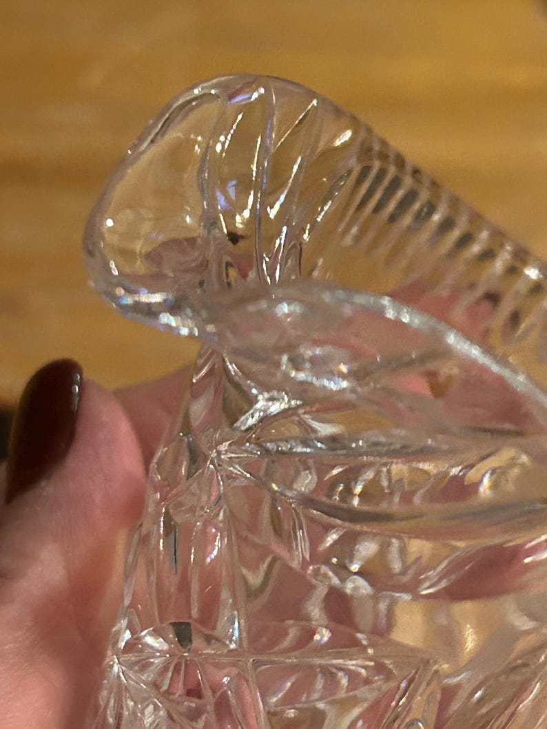 Op de afbeelding: Close-up van een heldere glazen kan met een decoratief, facetgeslepen ontwerp. De kan heeft een brede, uitlopende opening en een ronde basis.