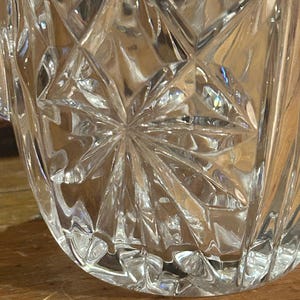 Op de afbeelding: Een heldere glazen vaas met een stervormig patroon. De vaas heeft een brede opening en een ronde basis.