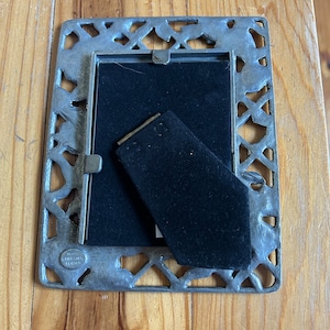 May include: A silver picture frame with an ornate design. The frame has a black velvet backing and a small metal tag with the text "Hallmark 1991" on it.