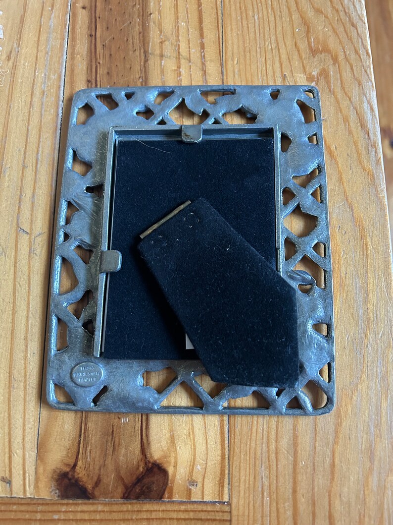 May include: A silver picture frame with an ornate design. The frame has a black velvet backing and a small metal tag with the text "Hallmark 1991" on it.