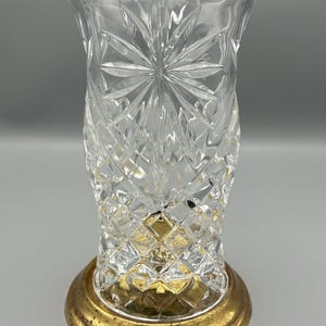 May include: A clear glass vase with a cut crystal design and a gold metal base.