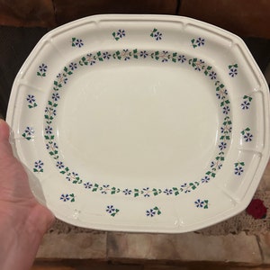 May include: A white oval serving platter with a decorative border of green leaves and blue flowers.