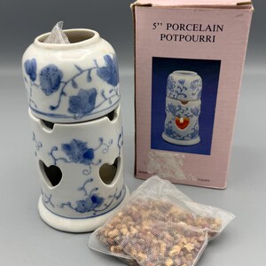 May include: A white porcelain potpourri burner with blue floral designs and heart-shaped cutouts. The burner is stacked with two pieces and comes with a sachet of potpourri. The box reads "5" PORCELAIN POTPOURRI".
