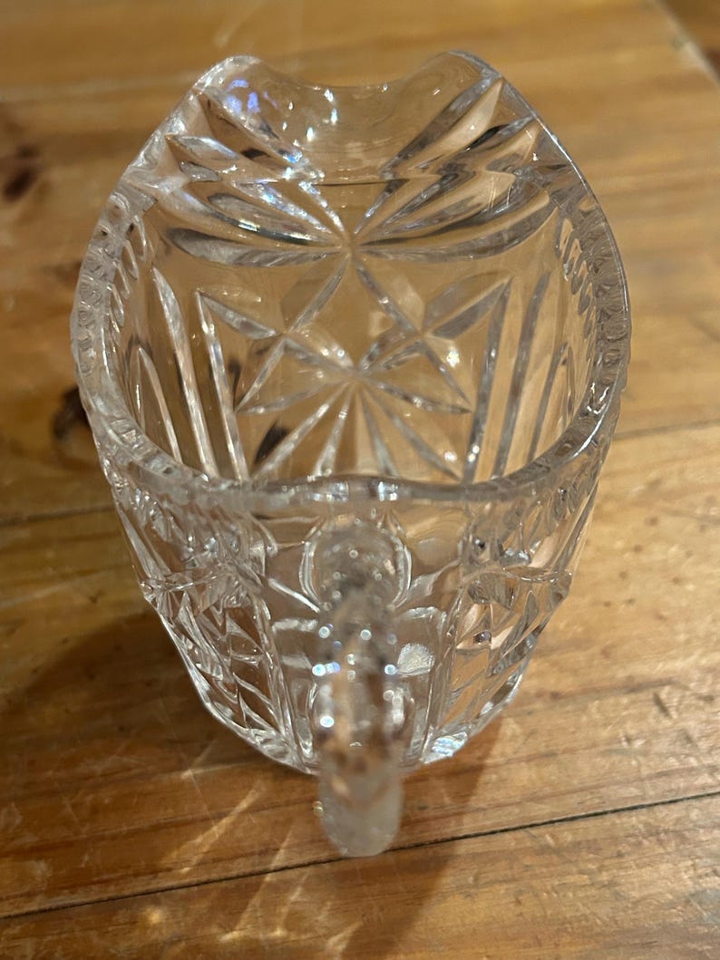 Op de afbeelding: Een glazen roomkan met een geslepen glasontwerp. De roomkan heeft een klein handvat.