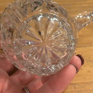 Op de afbeelding: Een glazen kan met een diamantpatroon. De kan heeft een handvat en een tuit.
