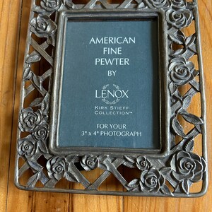 May include: A silver-toned pewter picture frame with a rose design. The frame is for a 3 x 4 inch photograph. It says "American Fine Pewter by Lenox Kirk Stieff Collection".