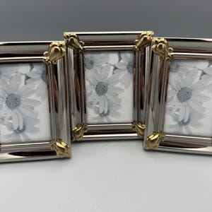May include: Three silver-toned picture frames with gold-colored corner accents. Each frame holds a black and white floral print. The frames are rectangular and have a polished finish, suitable for displaying photographs or artwork.
