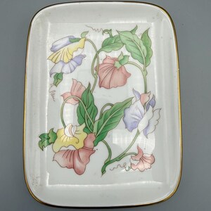 May include: A rectangular white ceramic dish with a gold rim. The dish is decorated with a floral design featuring pink, yellow, and purple flowers with green leaves. The flowers are arranged in a delicate pattern.