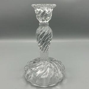 May include: A clear glass candle holder with a twisted design. The holder has a wide base and a narrow top.