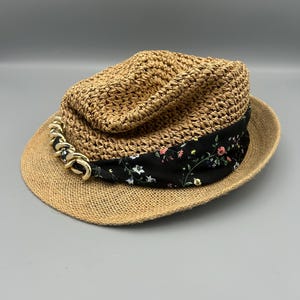 May include: A brown straw hat with a black and floral patterned band and a gold chain accent.