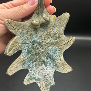 May include: A ceramic leaf dish with two acorns on the top. The leaf is green and blue with a textured surface.