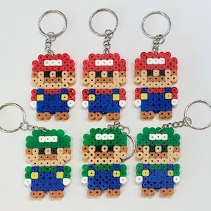May include: Five beaded keychains featuring characters from the Super Mario Bros. video game franchise. Two keychains feature Mario, wearing a red hat and blue overalls, and three keychains feature Luigi, wearing a green hat and blue overalls.