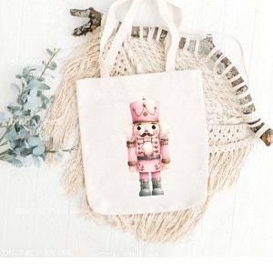 May include: A pink and white nutcracker with a gold belt and a black moustache. The nutcracker is standing on a white tote bag.