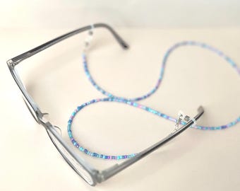 Könnte beinhalten: Eine Brille mit einer Perlenkette, die an den Bügeln befestigt ist. Die Kette besteht aus kleinen, bunten Perlen in Blautönen, Lila und Rosa.