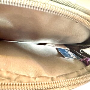 May include: Tan, round zippered case with a light-colored interior. The zipper is a matching tan color. A blue tag with the word "Disney" is visible inside the case.