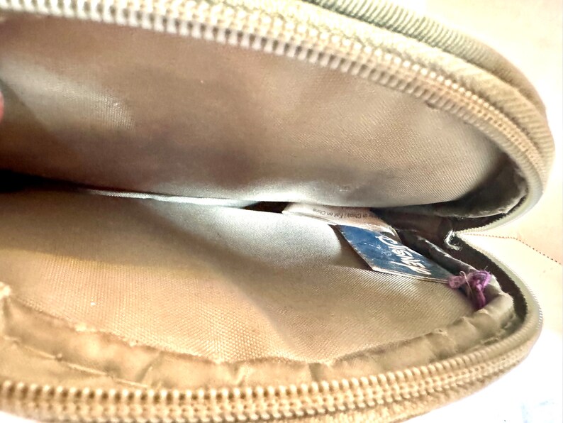 May include: Tan, round zippered case with a light-colored interior. The zipper is a matching tan color. A blue tag with the word "Disney" is visible inside the case.