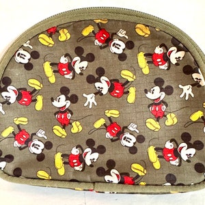 May include: A half-moon shaped cosmetic bag with a repeating pattern of Mickey Mouse in red, yellow, black, and white on a gray-green background. The bag has a green zipper and trim.