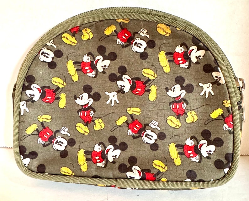 May include: A half-moon shaped cosmetic bag with a repeating pattern of Mickey Mouse in red, yellow, black, and white on a gray-green background. The bag has a green zipper and trim.