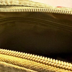May include: Close-up of an open, olive-green zippered pouch. The interior features a smaller zippered pocket and a light green lining. The main zipper is beige with a white pull.
