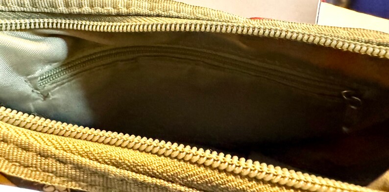 May include: Close-up of an open, olive-green zippered pouch. The interior features a smaller zippered pocket and a light green lining. The main zipper is beige with a white pull.
