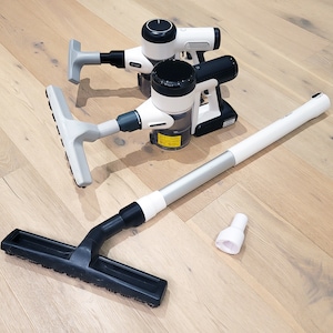 May include: Three white and black cordless vacuum cleaners with different attachments, including a long extension wand, a crevice tool, and a floor brush. The vacuum cleaners are on a light wood floor.