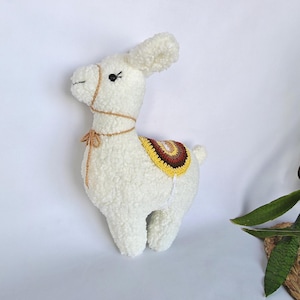 May include: White crocheted llama plush toy with a brown and yellow saddle.