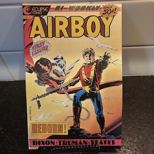May include: A comic book cover featuring a superhero called Airboy. The cover is yellow, red, and blue with the title "Airboy" in large yellow letters. The superhero is flying in the air with a gun in his hand. The text "Reborn!" is in a yellow box on the cover. The comic book is from Eclipse Comics and is issue number 1.