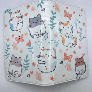 May include: White cat-themed planner cover with a light blue background. The cover features cartoon cats in various poses, along with pink butterflies, flowers, and hearts. The planner is designed with a stitched border.
