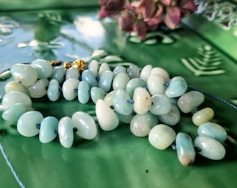 May include: A strand of light blue and white gemstone beads strung on a blue cord. The beads are smooth and oval-shaped.