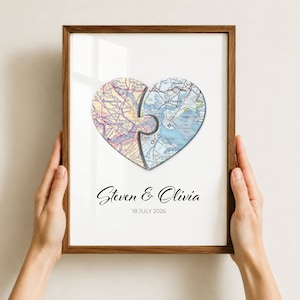 Puede incluir: Una impresión de arte mural enmarcada con dos segmentos de mapa en forma de piezas de rompecabezas que forman un corazón. El mapa muestra Somerville y Cambridge en tonos amarillos y azules. Debajo del corazón, el texto dice Steven & Olivia y 18 JULY 2026.
